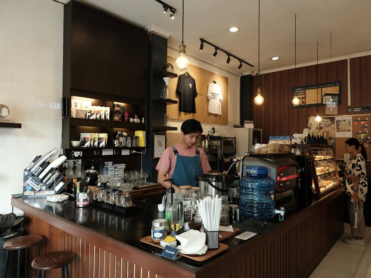 A barista working the espresso bar while a customer waits at the pastry case