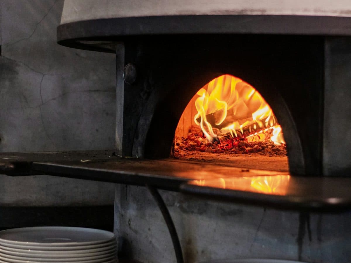 A wood-fired pizza oven burning, plates stacked ready beside it